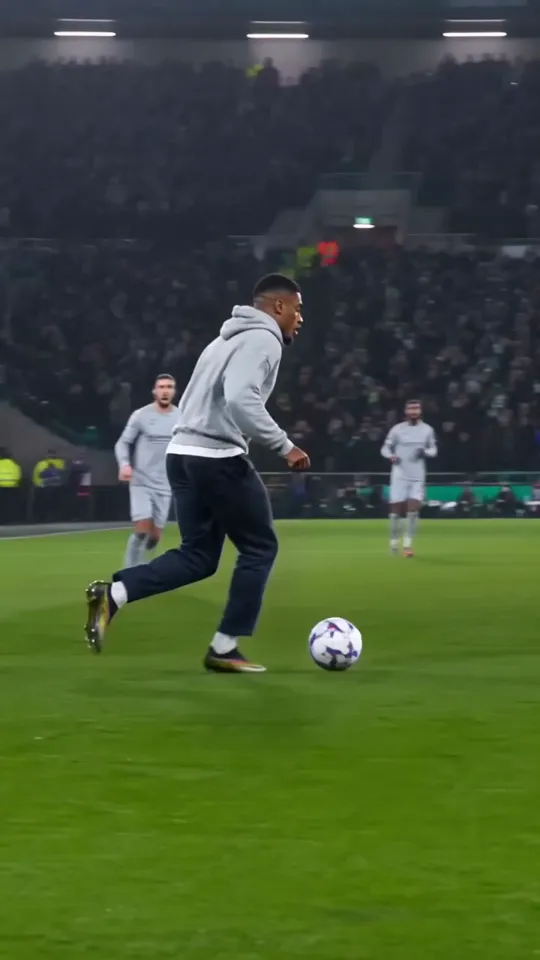 Ozil goal AI video frame: a man in a grey hoodie runs onto the ball in the box under the floodlights